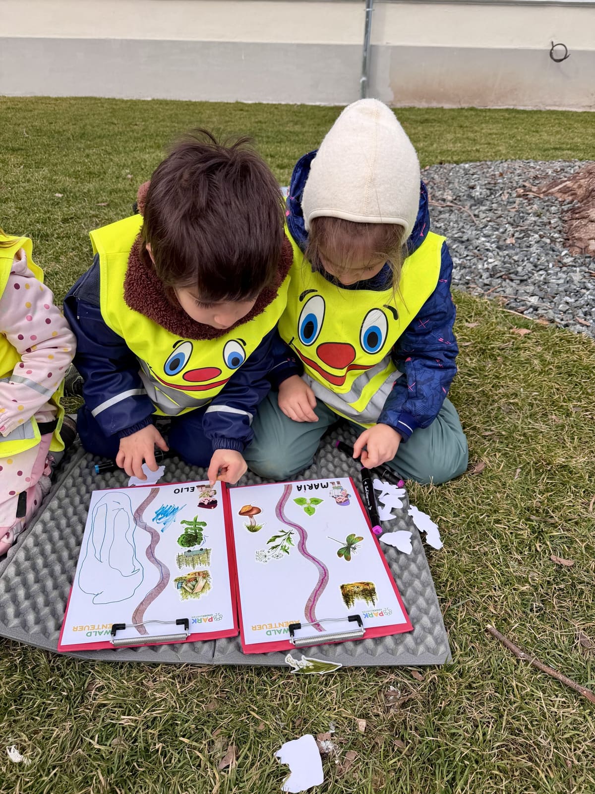 Zwei Kinder lösen Arbeitsblätter draußen auf der Wiese