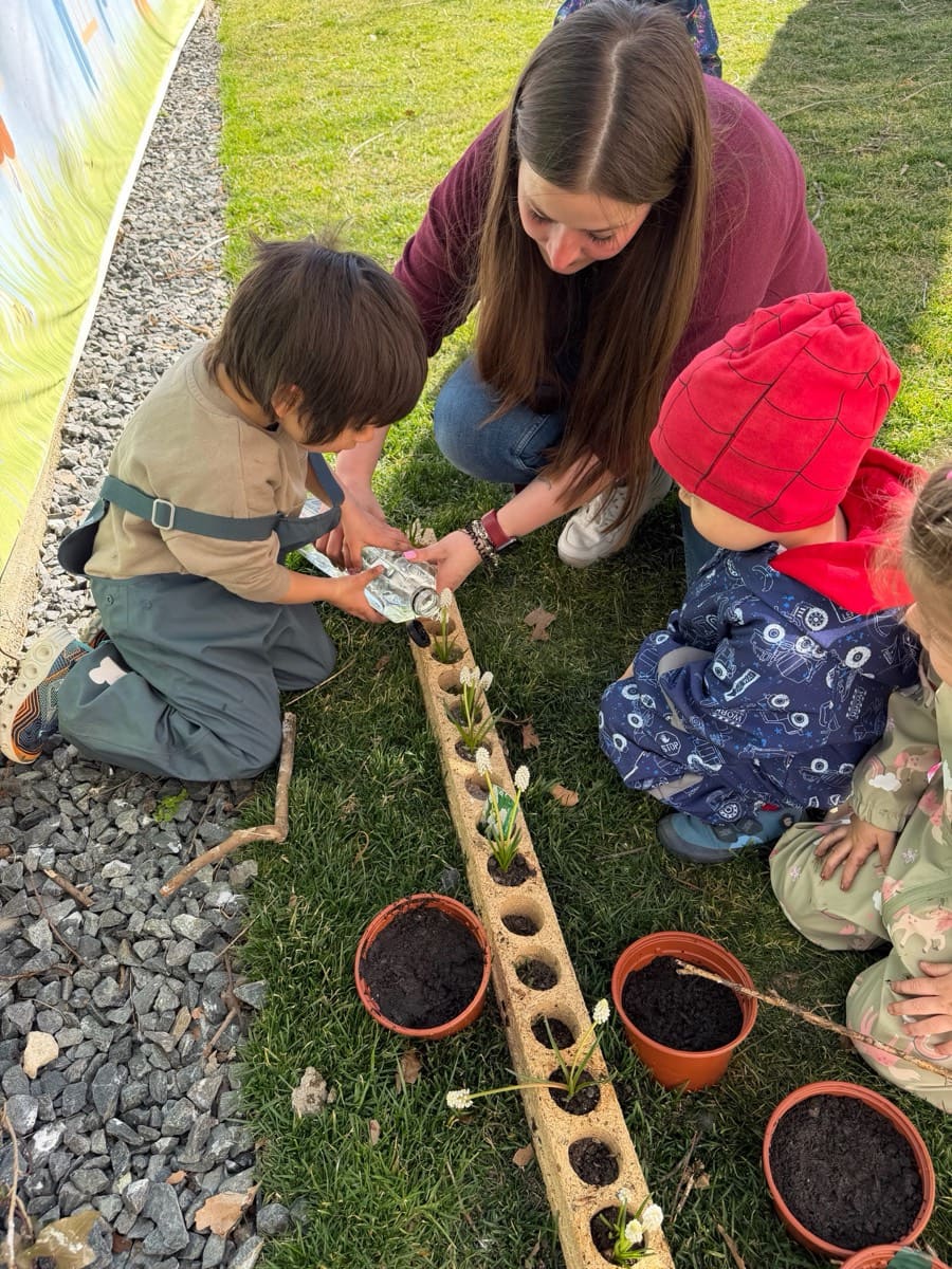 Kinder und Erzieherin pflanzen Blumen in Töpfe